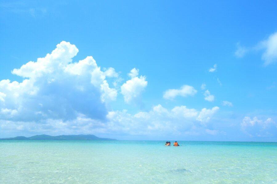 7月の久米島の遠浅の海で遊ぶ観光客と青空の風景